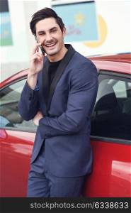 Portrait of an attractive young business man standing near a red car using his smartphone.