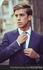 Portrait of an attractive young businessman in urban background wearing blue suit a necktie. Blonde hair