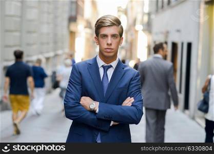 Portrait of an attractive young businessman in urban background wearing blue suit a necktie. Blonde hair