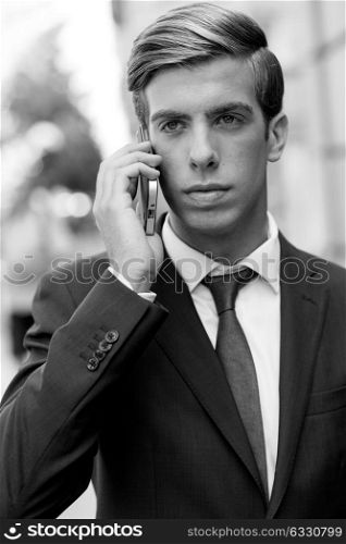 Portrait of an attractive young businessman on the phone in urban background, wearing blue suit and tie. Blonde hair