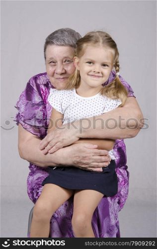 Portrait of an elderly woman of eighty years, on the lap of a woman sits granddaughter four years. Woman hugging a girl