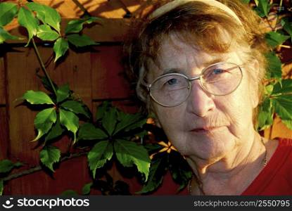 Portrait of an elderly woman outside with green vines