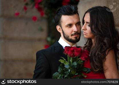 Portrait of an elegant fashion couple in love on a romantic date. Man giving a bouquet of red roses to a woman.
