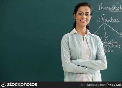 Portrait of an elementary school teacher with arms crossed standing against green board