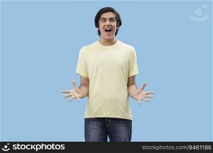Portrait of an excited teenage boy gesturing while standing against blue background