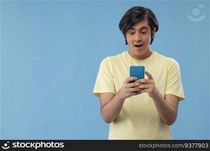 Portrait of an excited teenage boy using Smartphone while standing against blue background