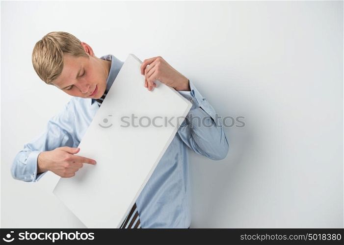 Portrait of an excited young businessman holding a blank board while leaning on wall at office