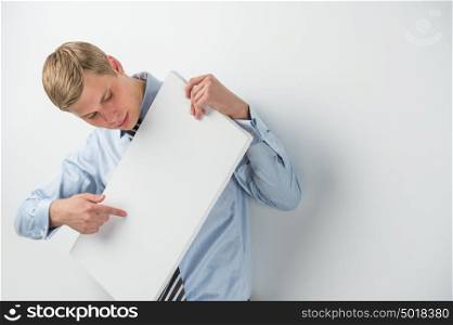 Portrait of an excited young businessman holding a blank board while leaning on wall at office