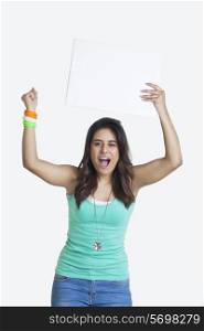 Portrait of an excited young woman cheering while holding blank placard over white background