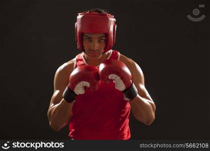 Portrait of an Indian boxer wearing gloves and head protector over black background