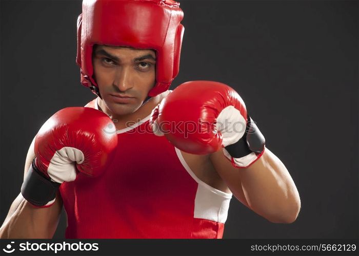 Portrait of an Indian male boxer wearing gloves and head protector against black background