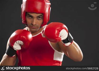 Portrait of an Indian male boxer wearing gloves and head protector against black background