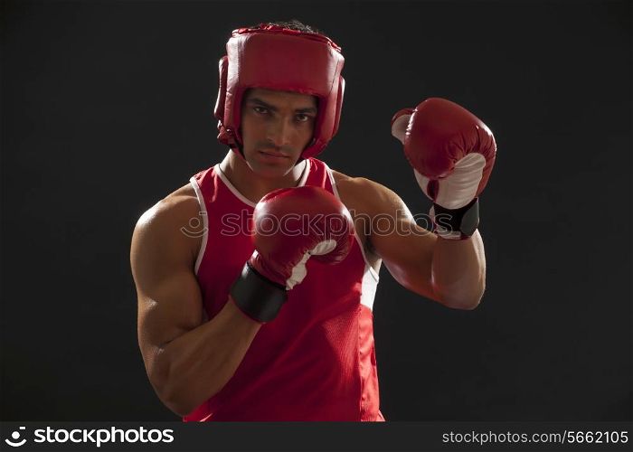 Portrait of an Indian male boxer wearing gloves and head protector isolated over black background