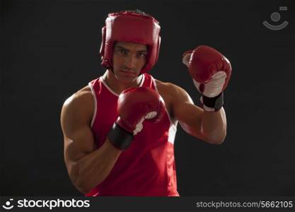 Portrait of an Indian male boxer wearing gloves and head protector isolated over black background