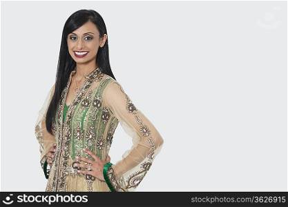 Portrait of an Indian woman in elegant designer wear standing with hands on hips over gray background