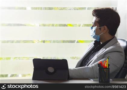 PORTRAIT OF AN OFFICE EXECUTIVE SITTING WITH MASK AND LOOKING OUTSIDE