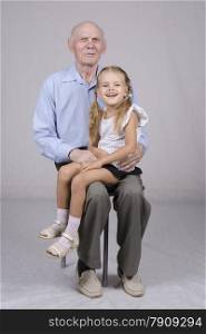 Portrait of an old man eighty years old, on the lap of a man sitting granddaughter four years.