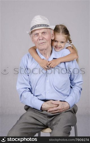 Portrait of an old man eighty years, the neck of a man hugs a four-year-old girl. Studio light background