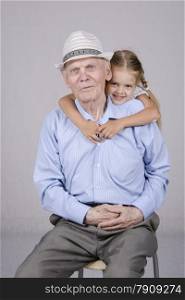 Portrait of an old man eighty years, the neck of a man hugs a four-year-old girl. Studio light background