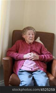 Portrait of an older lady sitting in an armchair in a care home talking to someone out of frame