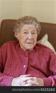 Portrait of an older lady sitting in an armchair in a care home looking straight to camera