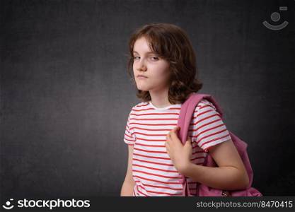 Portrait of an unhappy schoolgirl holding backpack, looking at camera. Unhappy schoolgirl holding backpack, looking at camera