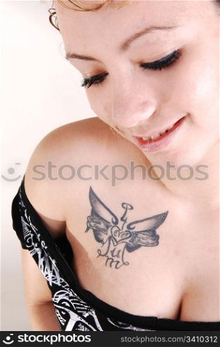 Portrait of an young pretty woman in a black sweater and an big tattooon her chest with nice boobs for light gray background