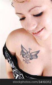 Portrait of an young pretty woman in a black sweater and an big tattooon her chest with nice boobs for light gray background
