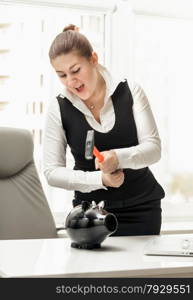 Portrait of angry businesswoman breaking piggy bank with hammer