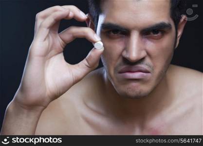 Portrait of angry drug addict holding pill against black background