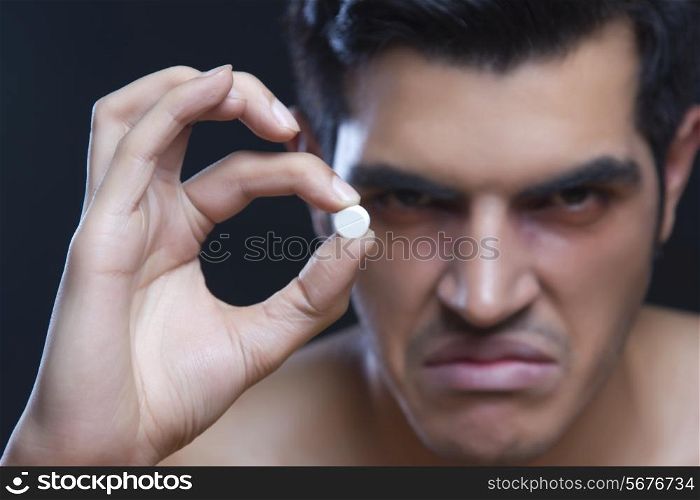 Portrait of angry male drug addict holding pill against black background