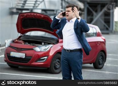 Portrait of angry man talking by phone because of broke down car