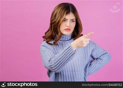 Portrait of angry sad young woman point index finger aside isolated over pink background. People lifestyle and emotion concept.