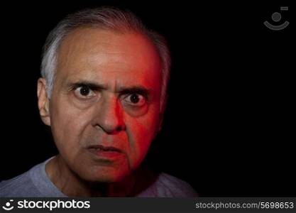 Portrait of angry senior man over black background