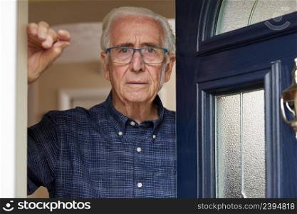 Portrait Of Anxious Senior Man At Home Looking Out Of Front Door