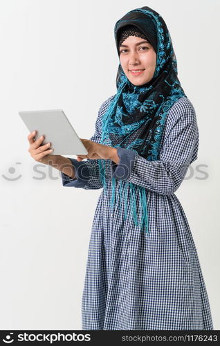 Portrait of Arabic muslim woman in colorful traditional clothes using laptop computer on white background.