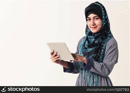 Portrait of Arabic muslim woman in colorful traditional clothes using laptop computer on white background.