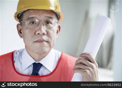 Portrait of architect in a hardhat holding a rolled up blueprint indoors, close-up