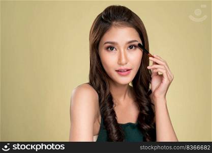Portrait of ardent young woman with healthy fair skin applying her eyeshadow with brush. Female model with fashion makeup. Beauty and makeup concept.. Portrait of ardent female model applying her eyeshadow and holding a mirror.