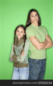 Portrait of Asian-American girl and teen boy standing back to back against green background.