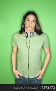 Portrait of Asian-American teen boy with headphones around neck and hands in pockets.