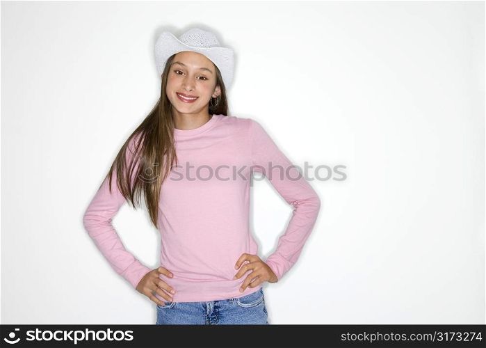 Portrait of Asian-American teen girl with cowboy hat and hands on hips standing in front of white background.