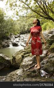 Portrait of Asian American woman in ethnic attire standing on rock by creek in Maui, Hawaii.