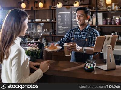 Portrait of asian barista hold take away coffee and Croissant cup and serving to customer in cafe with other barista working in background