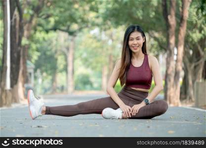 Portrait of Asian beautiful girl look at camera and smile when sit and stretch her leg on road in park or garden with day light.