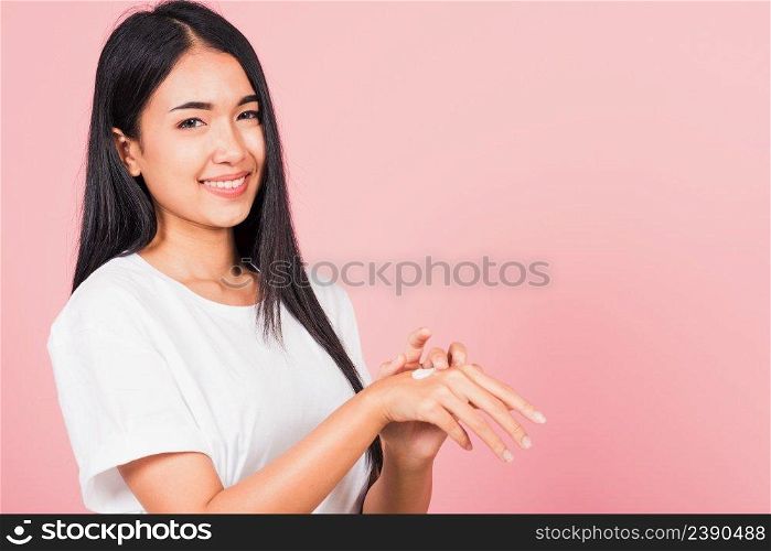 Portrait of Asian beautiful young woman applying lotion cosmetic moisturizer cream on her behind the palm skin back hand, studio shot isolated on pink background,  Hygiene skin body care concept