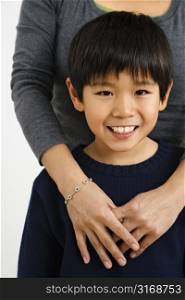 Portrait of Asian boy smiling with mother standing behind with arms around him.