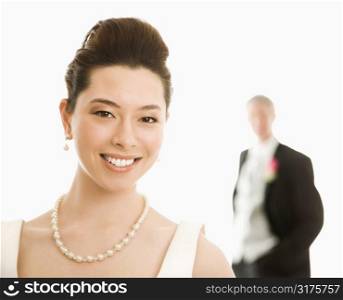 Portrait of Asian bride in foreground and Caucasian groom in background.