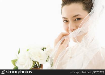 Portrait of Asian bride with bouquet and pulling veil over face.