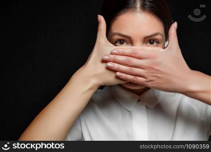 portrait of Asian brunette woman in white shirt with mouth covered by hand on black background